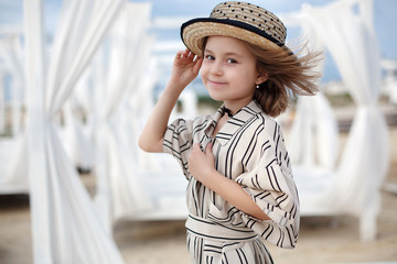 Small (8 years old) pretty cheerful girl in a white striped dress and in pink sunglasses stands on a wooden white pier.8 years old girl resting on the tropical beach alone on a warm sunny day.Child po