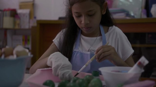 Asian cute girl is making crafts from egg shells on the desk, Young girl is coloring egg shells at home for her homework, Education concept.