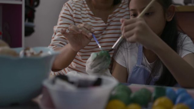 Asian girl and her mother are making crafts from the egg shells, Mother helping her daughter painting egg shells together at home, Education concept.