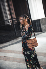 Happy young beautiful woman walking in city street Stylish fashion model wearing floral print dress
