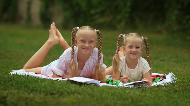 Older sister is engaged with the younger sister preparing her for school lying on a grass in a backyard in sunny day