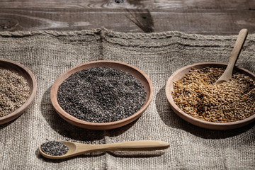 Sesame, chia and flax seeds in wooden dishes, wooden spoon with chia on wooden base.