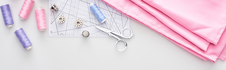 panoramic shot of fabric, sewing pattern, scissors, thimbles, bobbins and threads on white background
