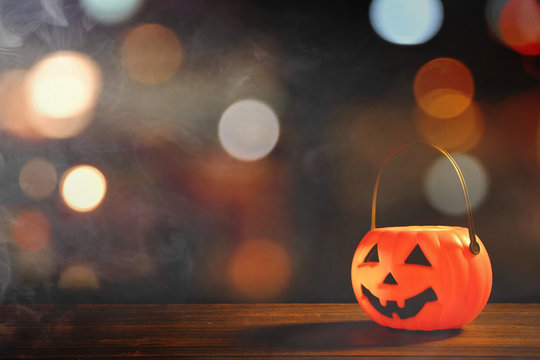 Halloween concept - Orange plastic pumpkin lantern on a dark wooden table with blurry sparkling light in the background, trick or treat, close up.