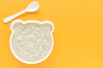Bear shape funny plate with oatmeal porridge, healthy baby or kids meal, fun food, top view on yellow background, copy space.