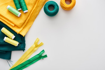 top view of fabric, knitting yarn balls, zippers and threads on white background