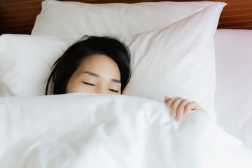 Woman stretching in bed after waking up, back view. Woman sitting near the big white window while stretching on bed after waking up with sunrise at morning, back view.