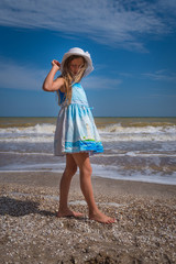 Beautiful seascape. The girl the blonde in a blue dress and a white hat in hand walks along the shore