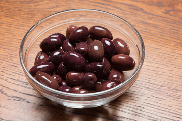 pink pickled olives in a glass bowl, on a wooden table, closeup