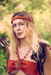 Beautiful girl archer with long blond hair with a bow and arrows dressed in leather