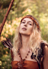 Beautiful girl archer with long blond hair with a bow and arrows dressed in leather
