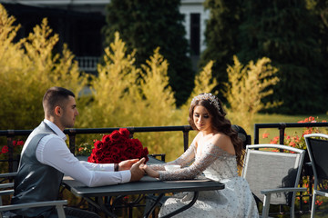 Young happy couple at cafe having conversation. Boyfriend and girlfriend in love enjoy together. Romantic date. Near to a table a bouquet of red roses