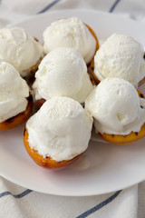 Homemade grilled peaches with vanilla ice cream on a white plate, low angle view. Closeup.