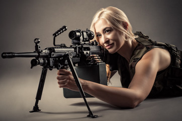 Obraz na płótnie Canvas beautiful blond woman aiming machine gun while lying on the floor