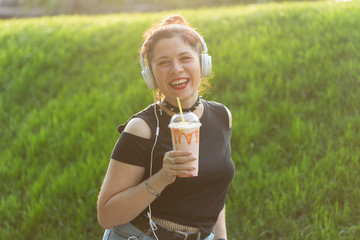 Portrait of a positive young pretty girl in punk clothes and glasses with a milkshake in her hands posing in a summer park on a warm summer evening. Vacation getaway concept.