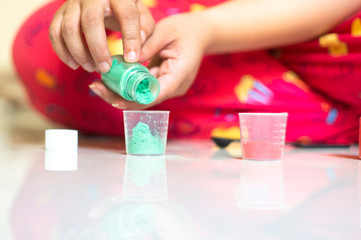 Young girl putting in mica color colourant into transparent measuring cups for making homemade hand made soap