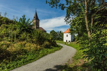 Fototapeta na wymiar Krasikov, Kokasice / Czech Republic - August 9 2019: View of the church of Mary Magdalene and a bell tower. Bright sunny day with blue sky and white clouds. Gravel footh path leading to church.