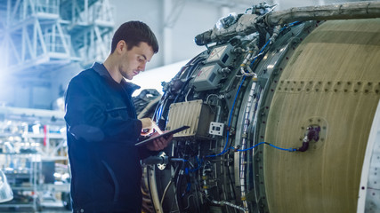 Aircraft Maintenance Mechanic Inspecting and Working on Airplane Jet Engine in Hangar