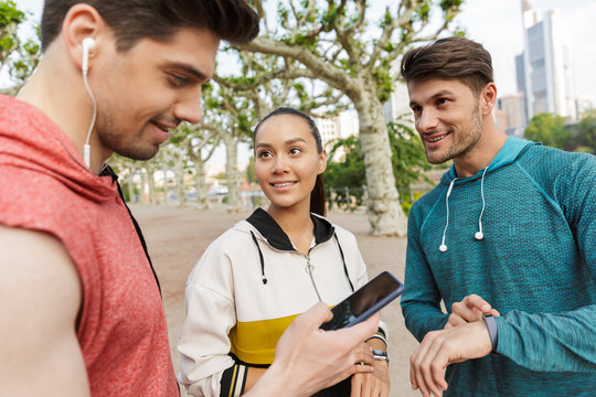 Photo of sporty smiling people using stopwatch and cellphone while working out in city park - Powered by Adobe