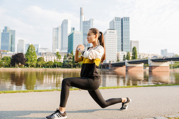 Fototapeta na wymiar Photo of young concentrated woman doing exercise while working out near city riverfront