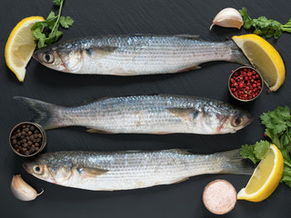 Fresh mullet on a stone black background with spices and lemon, seasoned with salt and pink pepper. View from above. Top View. Sea fish.