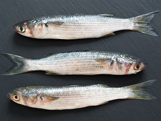 Fresh mullet is located on a black stone background. View from above. Sea fish.