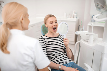 Dentists patient looking at her teeth in the mirror.
