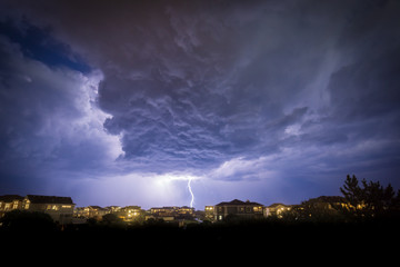 An offshore summer rain squall drops a bolt of lightning onto the ocean just off the coast of...