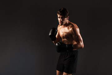 Obraz na płótnie Canvas Handsome young strong sportsman boxer in gloves make exercises boxing isolated over black wall background.