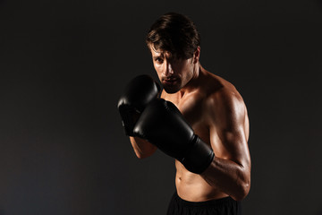 Handsome young strong sportsman boxer in gloves make exercises boxing isolated over black wall background.