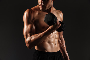 Fototapeta na wymiar Concentrated handsome young strong sportsman posing isolated over black wall background holding dumbbells.