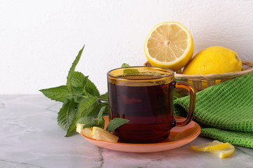 Glass of tea with mint and lemon on marble table.