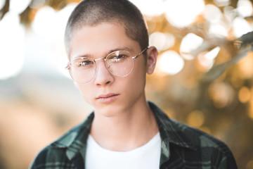 Teenage boy 16-18 year old wearing glasses outdoors over nature background. Looking at camera. Teenagerhood. Vision concept.