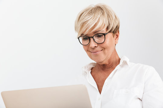 Image closeup of blond adult woman wearing eyeglasses smiling while using laptop computer