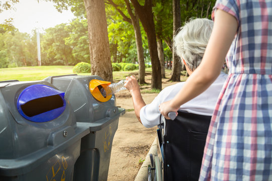 Asian senior woman hand holding plastic bottle,putting plastic water bottle in recycling bin,elderly tourist hand throwing garbage in a trash bin on street in park,environmental protection concept