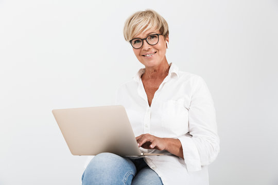 Image of beautiful adult woman wearing eyeglasses and earpods sitting with laptop computer