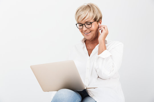 Image of smiling adult woman wearing eyeglasses and earpods sitting with laptop computer