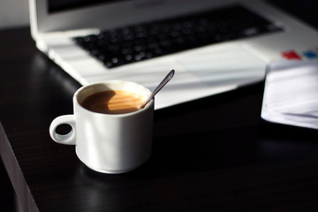 Coffee mug on a desk, with a laptop and a notebook.