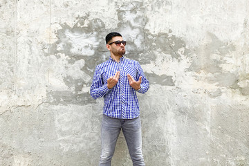 This is me. Portrait of proud handsome bearded young man in checkered blue shirt and sunglasses standing against concrete gray wall. showing himself and looking with proud haughty face.