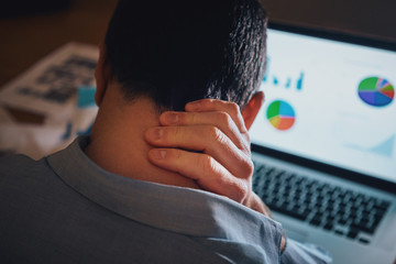 Male freelancer working on laptop suffering from neck pain