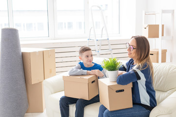 Cute mom and little boy son sort boxes with things after the move. The concept of housewarming mortgage and the joy of new housing.