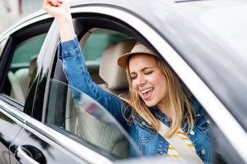 Young woman with hat sitting in car, listening to music and dancing.