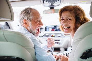 Rear view of happy senior couple sitting in car, looking back.
