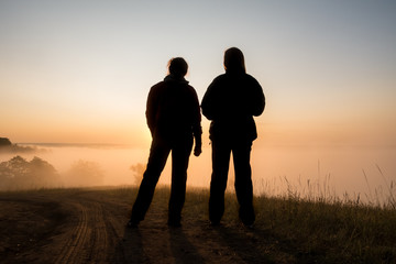 Fototapeta na wymiar silhouette of two peple looking at sunrise on foggy valley