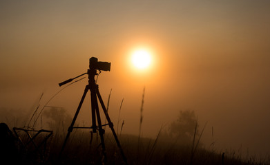Silhouette of photo camera on sunrise in the fog