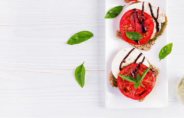 Sandwiches with mozzarella, tomatoes and rye bread on white wooden table. Top view