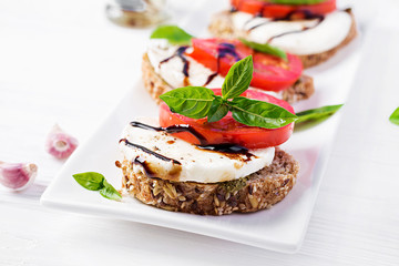 Sandwiches with mozzarella, tomatoes and rye bread on white wooden table.