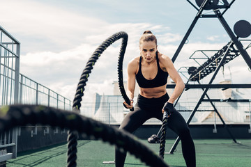 Woman in fitness wear working out with two battle ropes on rooftop © Artem Varnitsin