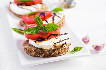Sandwiches with mozzarella, tomatoes and rye bread on white wooden table.