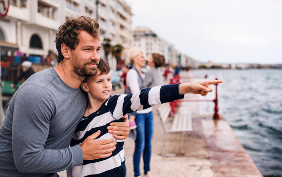 Father With Small Son Standing Outdoors In Town By The Sea, Talking.